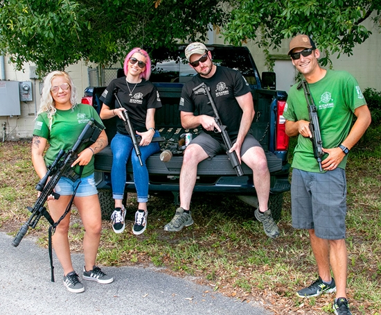 Group of Men and Women Holding Firearms and Wearing M*CARBO Shirts